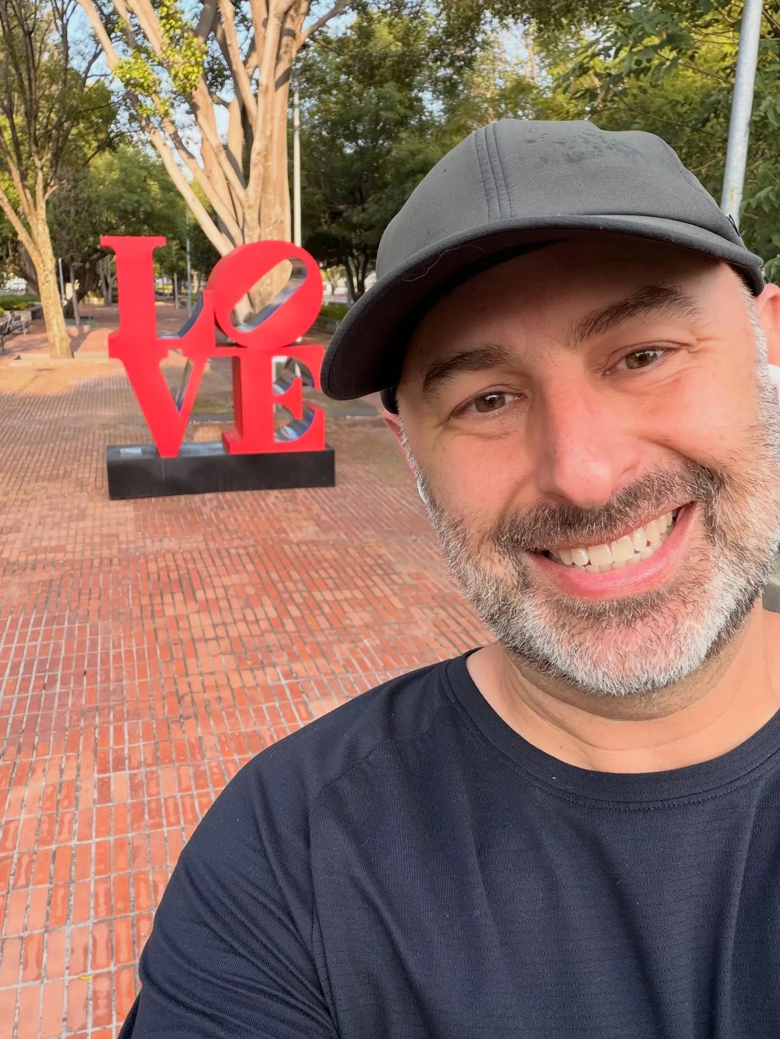 Aaron smiling in a park in front of a red LOVE sculpture
