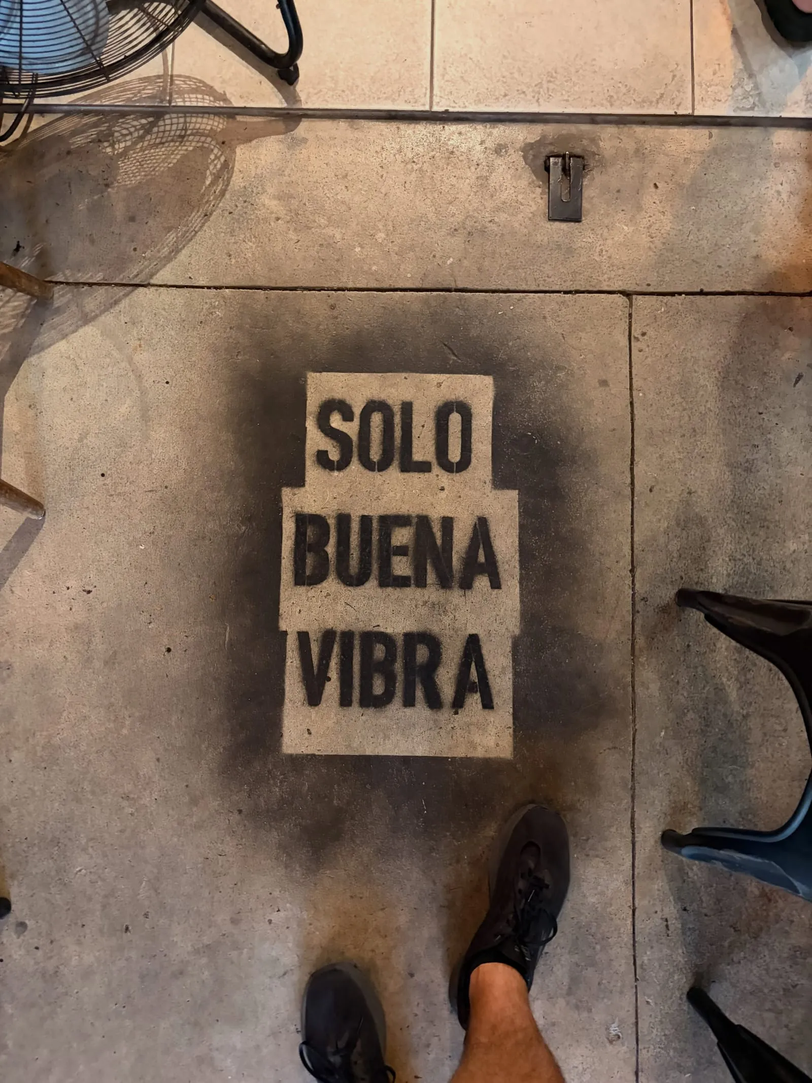 A stenciled sign on the pavement reading "Solo buena vibra," with Aaron's sneakers at the edge of the frame