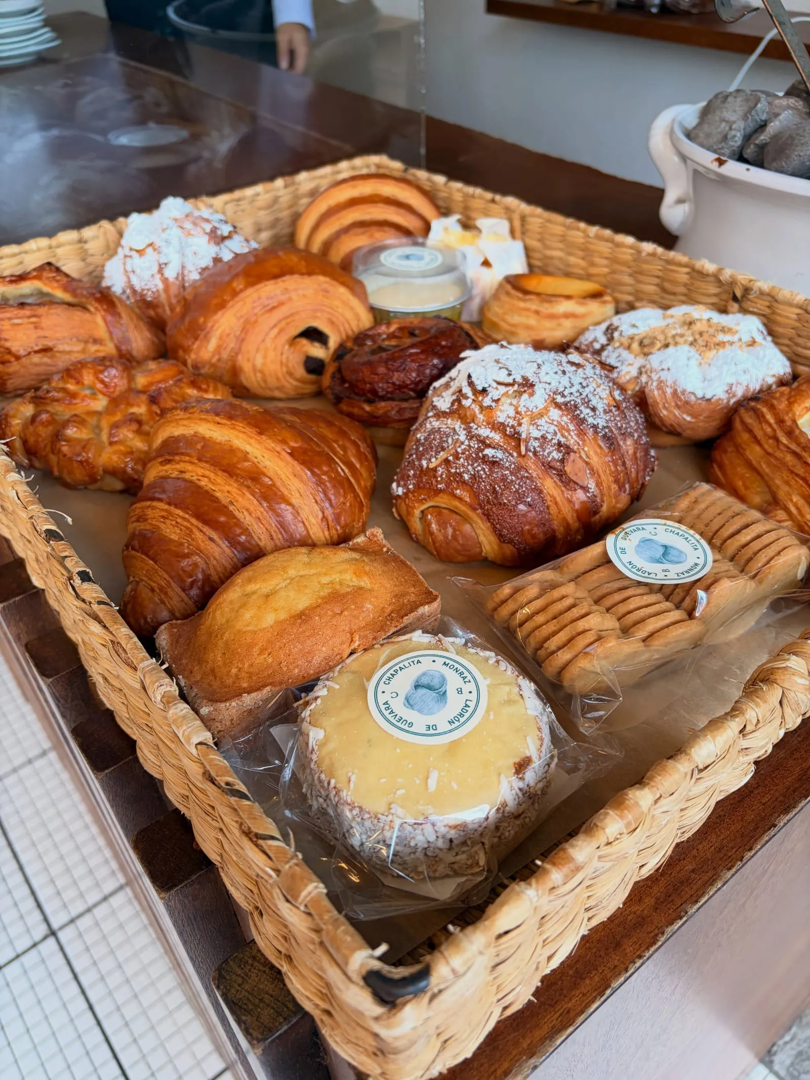 A basket of croissants, pain au chocolat, and other pastries at a bakery counter