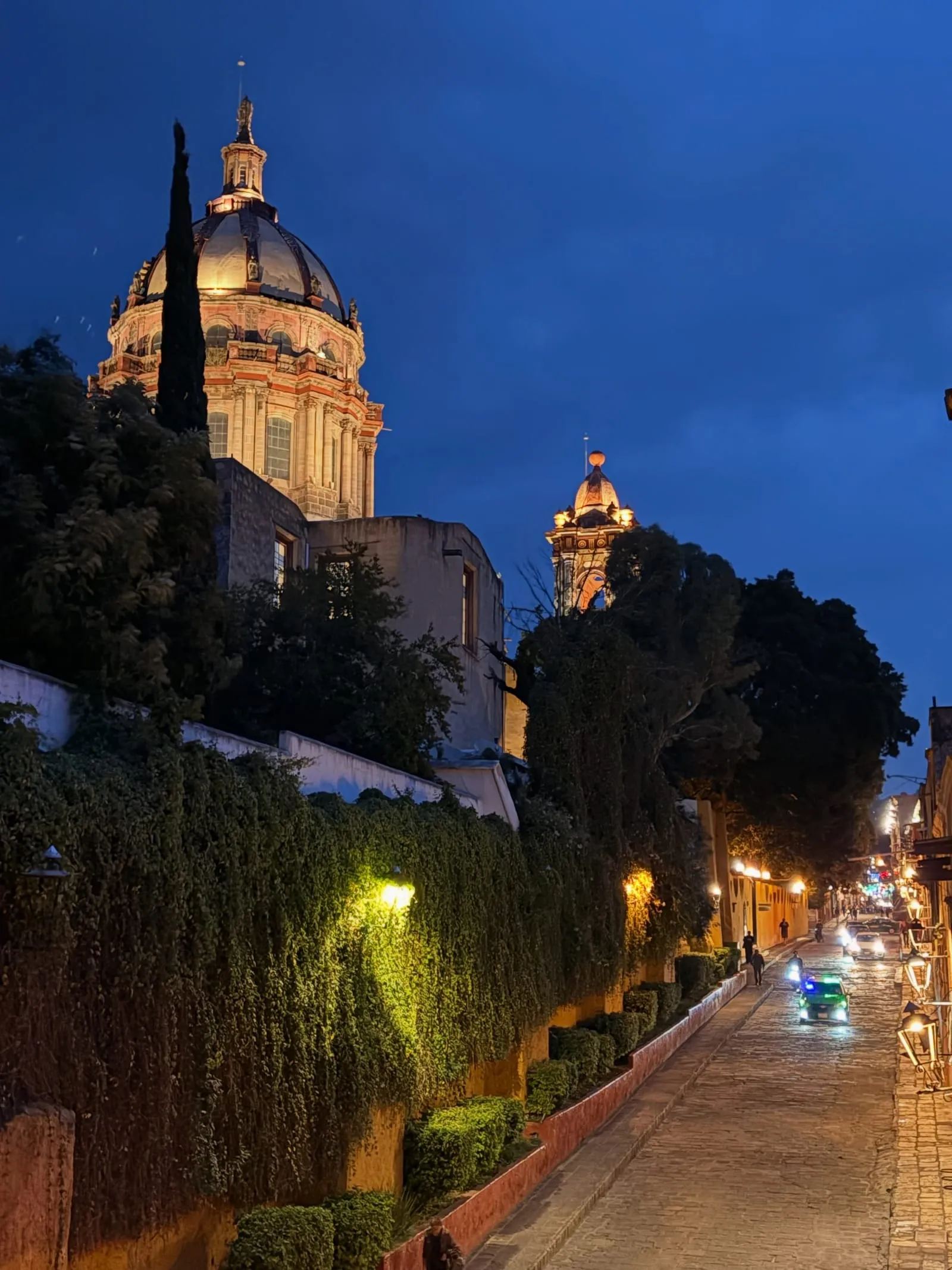 A lit church dome above a quiet street at dusk