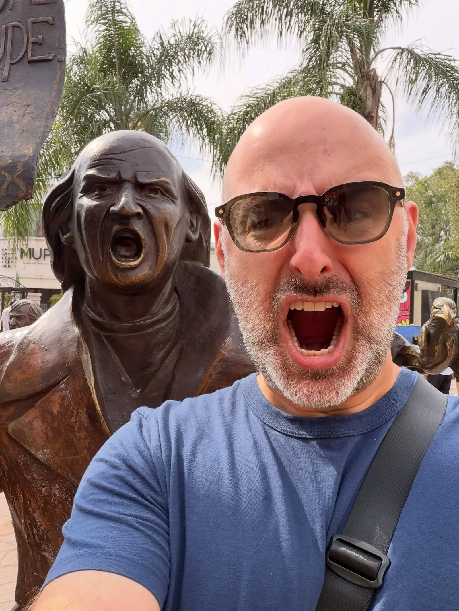 Aaron in sunglasses, mouth wide open, mimicking the shouting face of a bronze statue beside him
