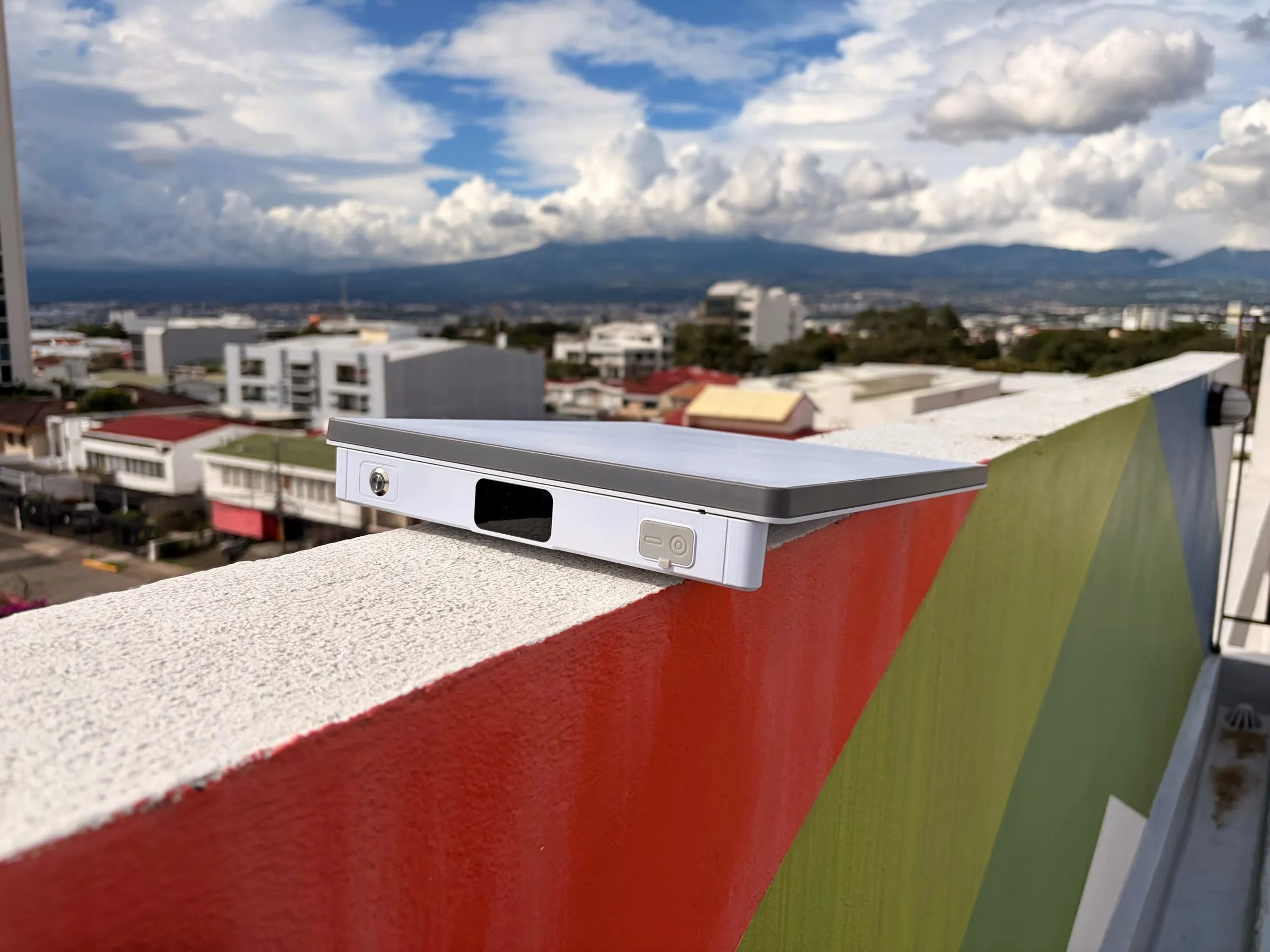 A Starlink Mini with the PeakDo LinkPower 2 attached, sitting on a rooftop ledge above San José with mountains and clouds behind it